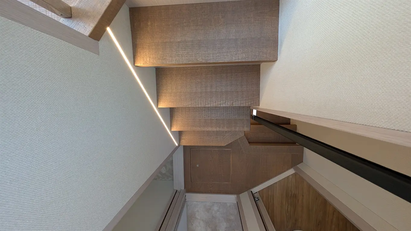 Modern wooden staircase with ambient lighting, leading down to a room with wooden flooring and a door on the left.
